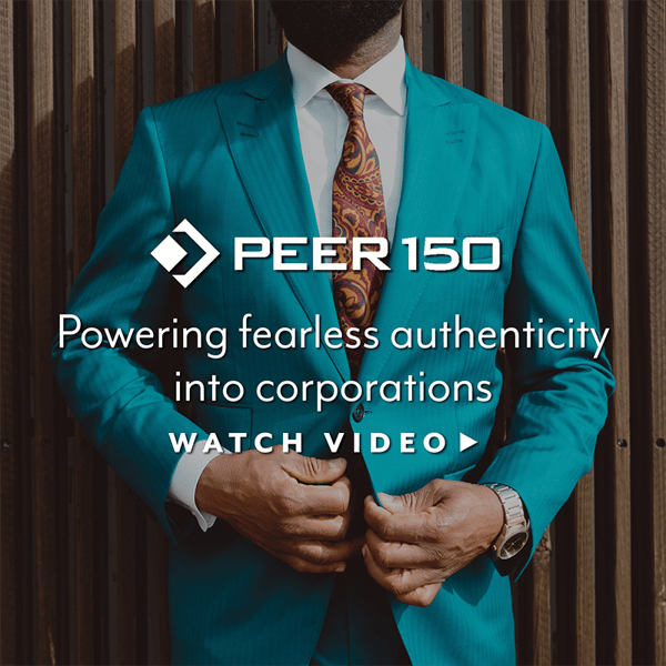 Man wearing teal blue suit and paisley print tie leaning on wood slatted wall